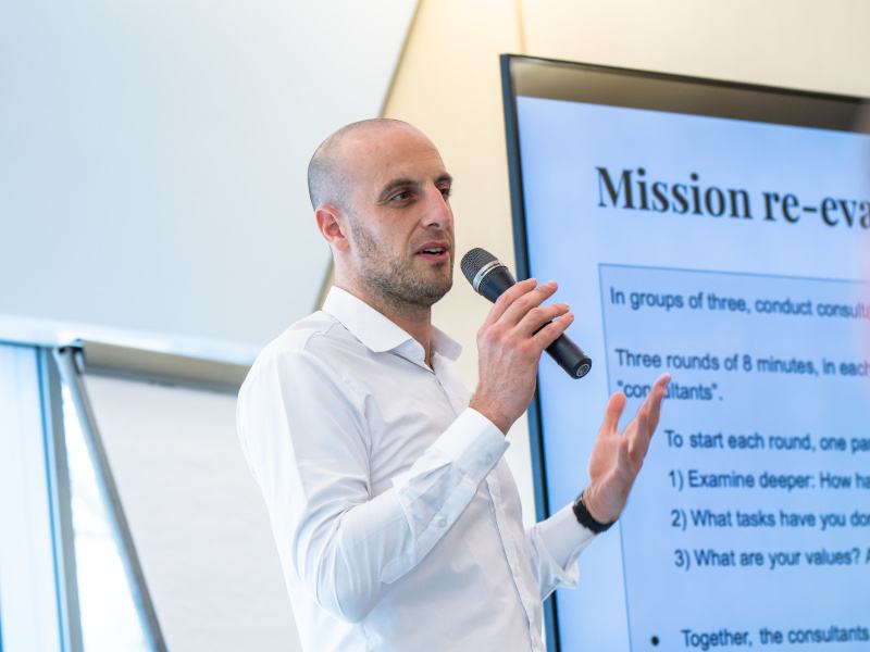 Dr Sami Asad in a white shirt gives a lecture in front of a screen and holds a microphone.