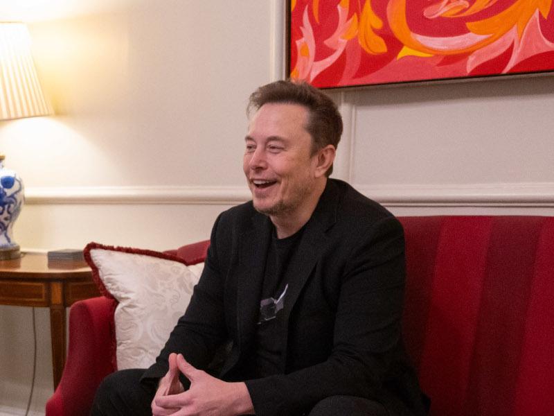 Elon Musk sitting on a chair and laughing.