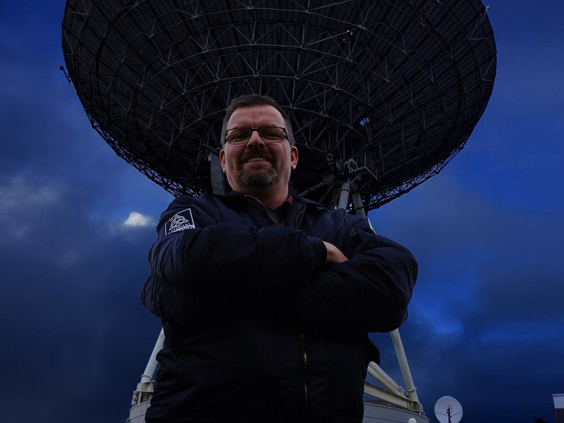 Bruce Hannah from the NSC standing in front of a large satellite dish.