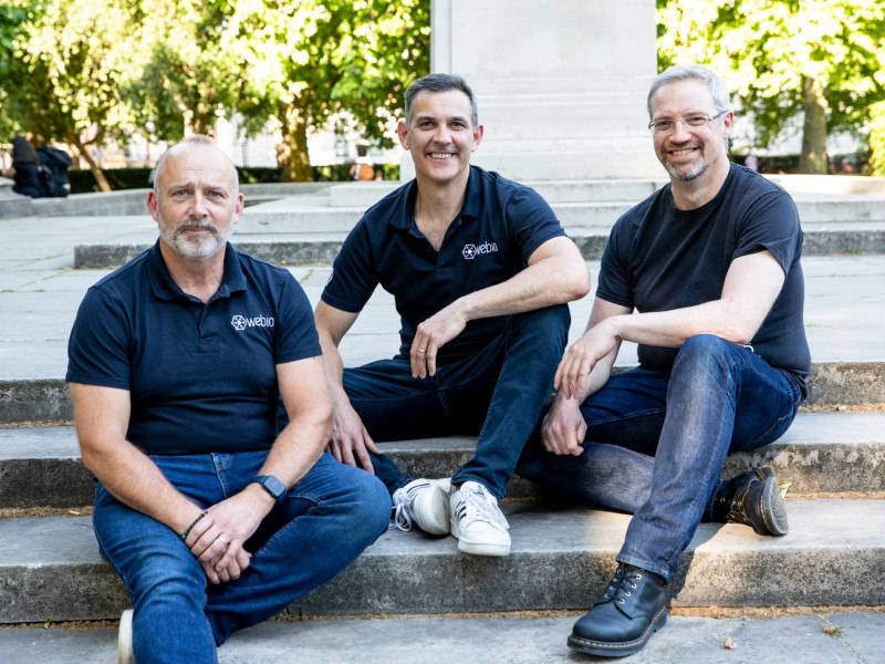 Webio co-founders sitting on stairs outdoors. Each of them wears a T-shirt with the Webio logo on them.