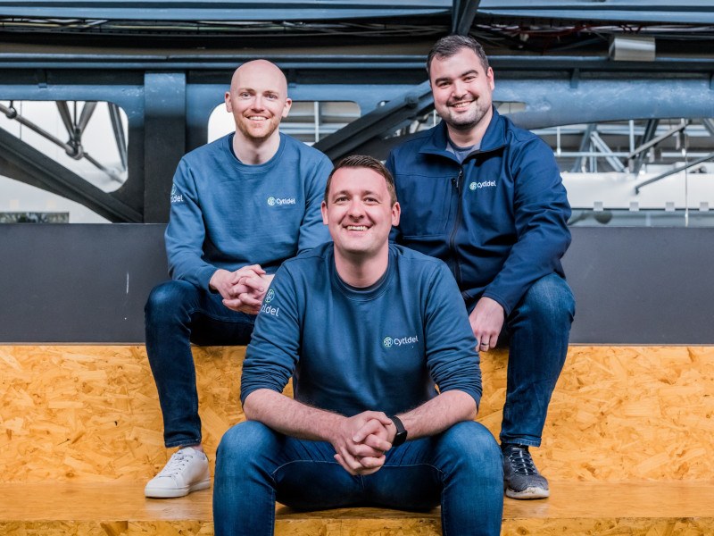 Three men wearing Cytidel jumpers seated in an indoor space.