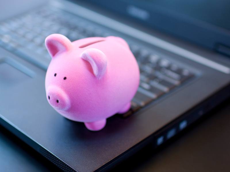 A pink piggy bank sits on top of a black laptop, symbolising finance and fintech.