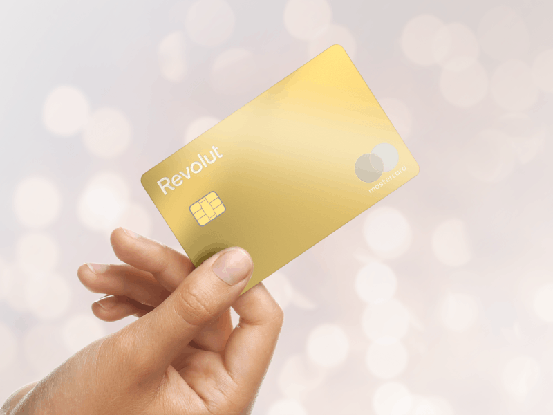 The Revolut logo on a gold debit card, held in a person's hand.