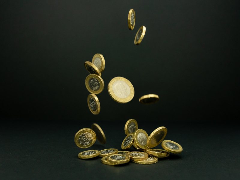 A pile of pound coins falling onto the ground in a dark background.