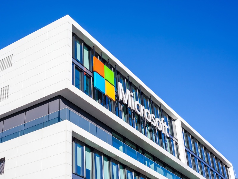 The Microsoft logo on the side of a tall building, with a clear blue sky behind it.