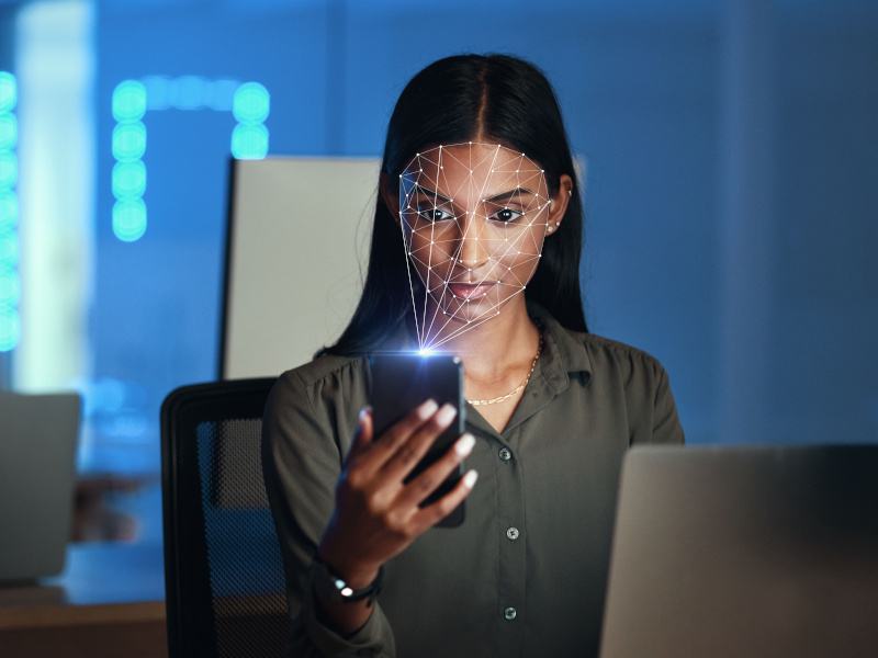 A woman looking at a phone with a light scanning her face. Used for the concept of Meta using facial recognition technology.