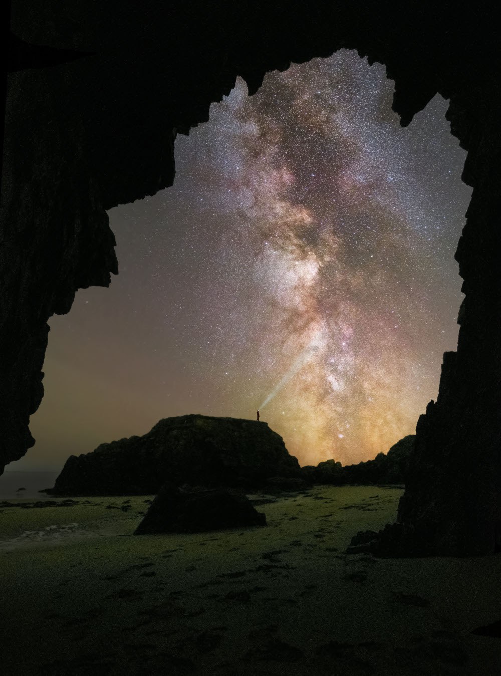 Una fotografía oscura tomada dentro de una cueva que muestra la Vía Láctea iluminando el cielo nocturno.