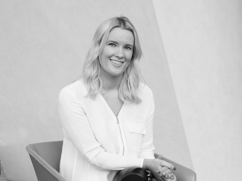 A black-and-white image of a woman sitting on a chair. She is Zara Flynn.