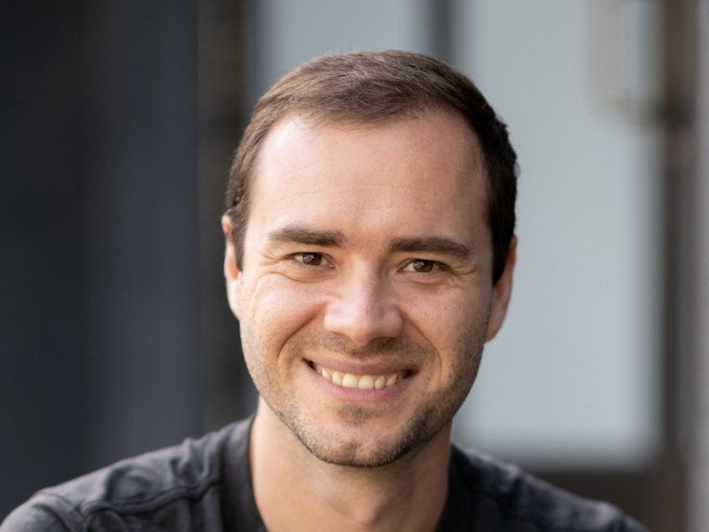 Headshot of Andrej Karpathy smiling. The background is blurred.