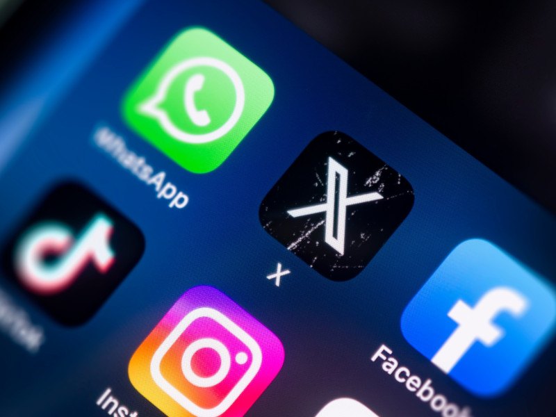 X app on a smartphone screen alongside other social media apps like WhatsApp and Facebook.