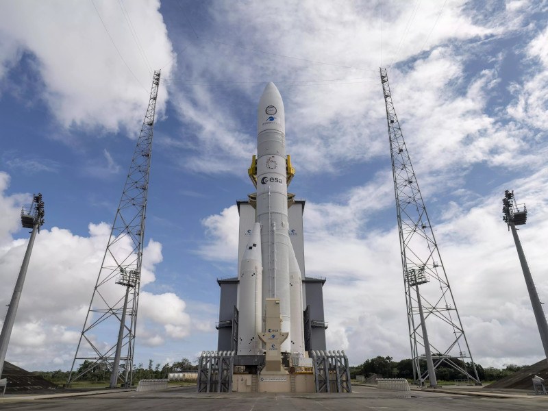 The ESA Ariane 6 rocket sits on the launch pad against a blue sky with clouds,
