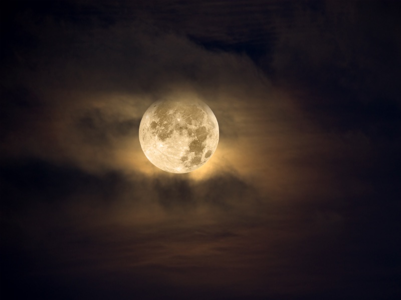 The moon glowing behind wispy clouds at night.