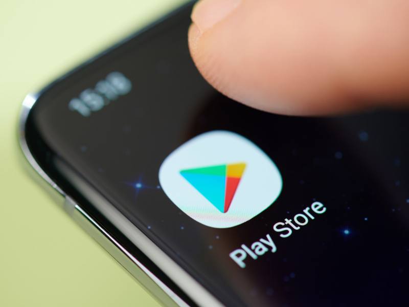 The Google Play Store logo on a smartphone screen with a person's finger over it.