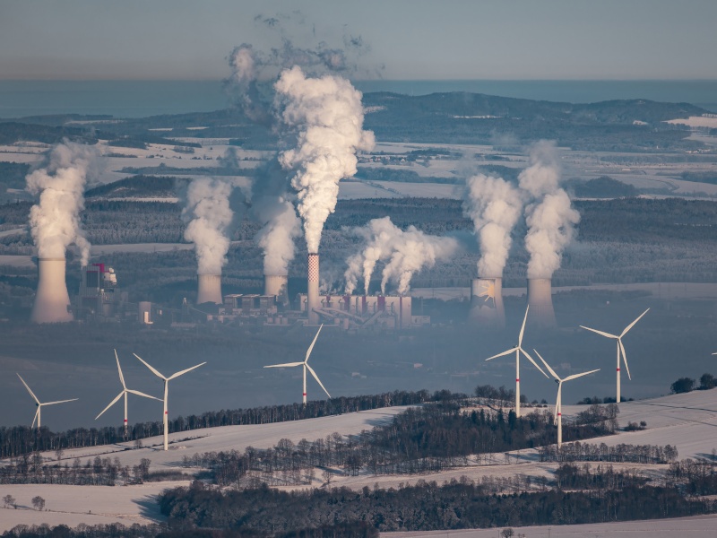 A landscape with multiple wind turbines and a power plant releasing smoke in the distance.