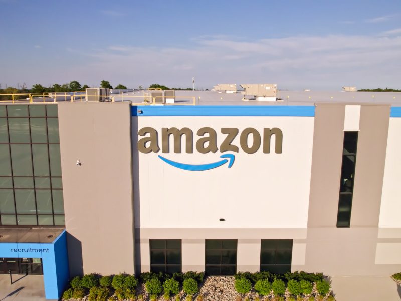 A large white building with Amazon's logo on the front with evening sun covering it.