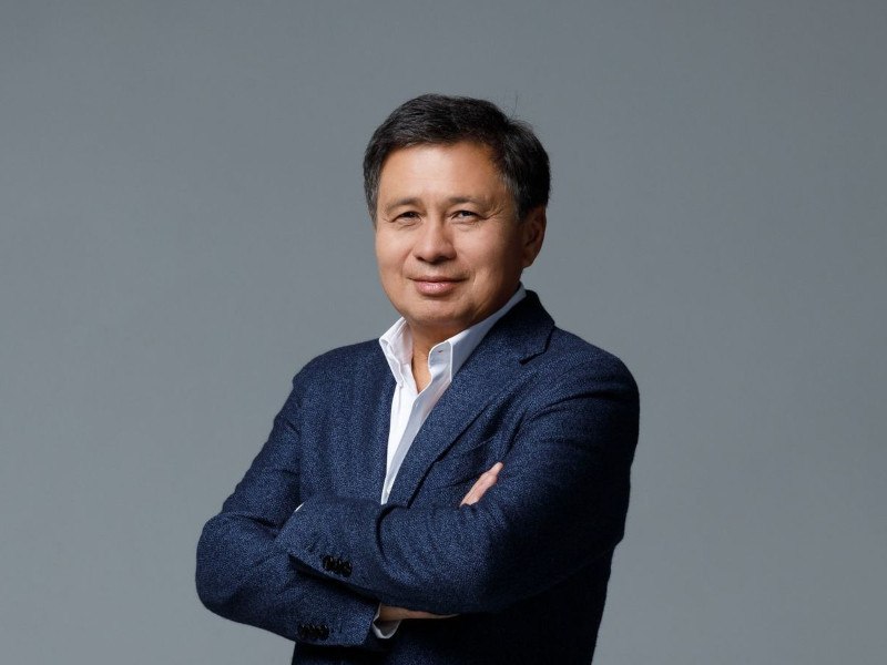 A photo of Murat Abdrakhmanov . He stands with his arms folded, smiling at the camera, against a grey background.