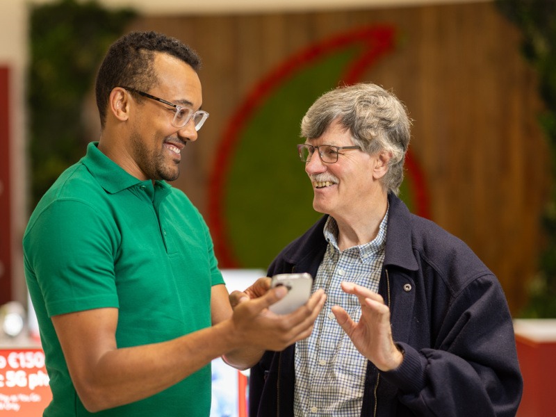 Two men standing together with one holding a phone in his hand. One of them is part of the Vodafone Hi Digital programme.