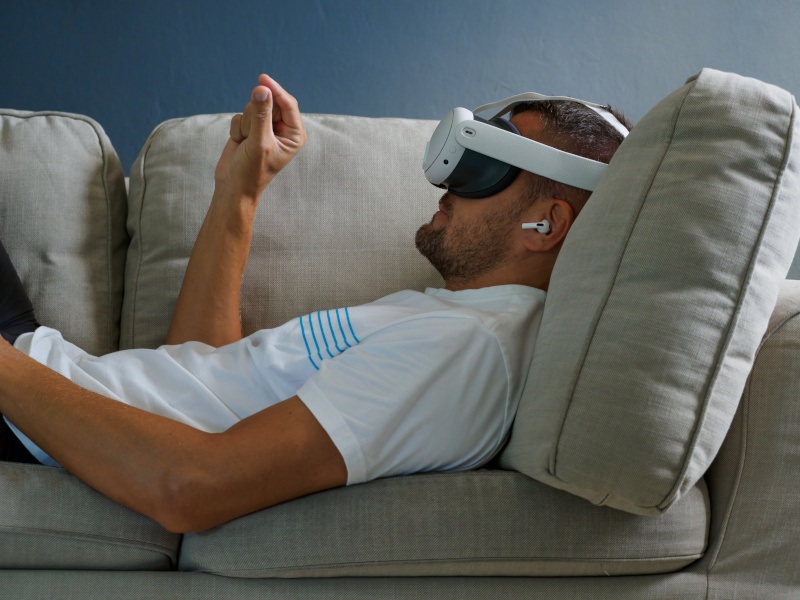 Man wearing a virtual reality headset and lying on a sofa.