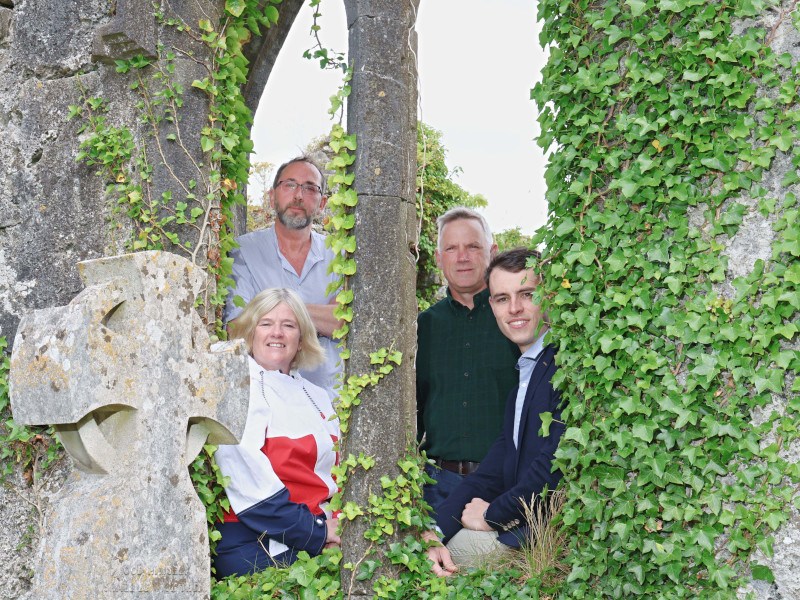 Three men and a woman standing in front of the window of a memorial site in Galway.