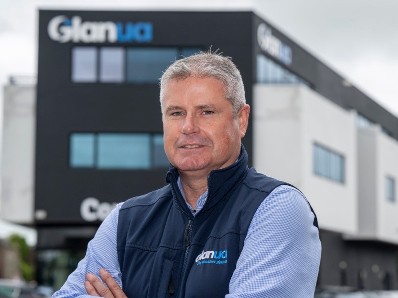 A man standing with his arms crossed in front of a building with the Glanua logo on the side.