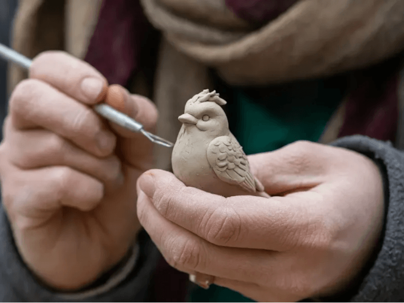 An AI-generated image of a person creating a clay sculpture of a bird. Created by Imagen 3.