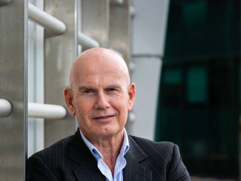 An image of Integrity360 executive chair Ian Brown, wearing a black suit and leaning by a railing.