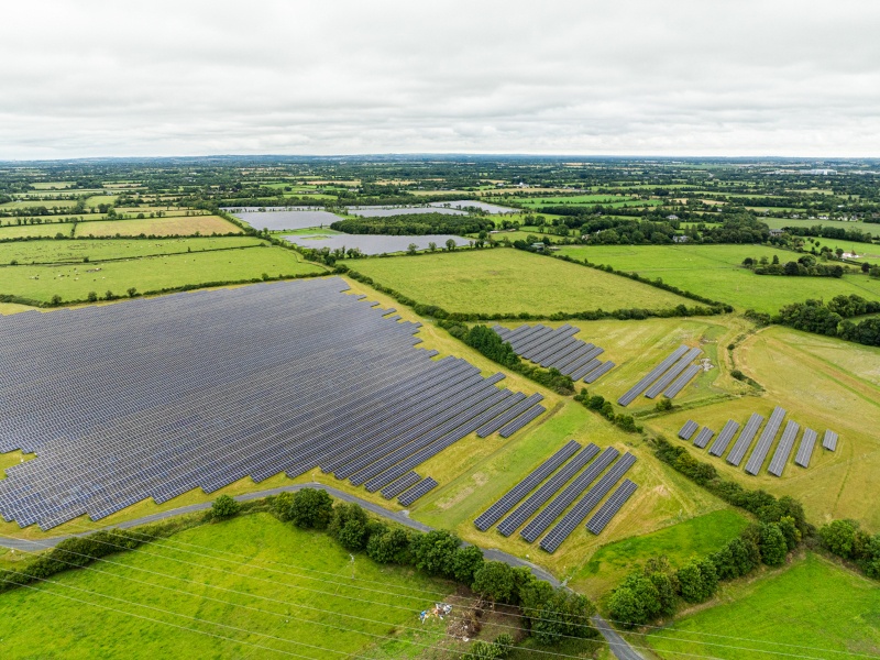 An aerial view of a solar farm in Meath, with fields and grey clouds in the background. This solar farm was acquired by Greencoat Renewables.