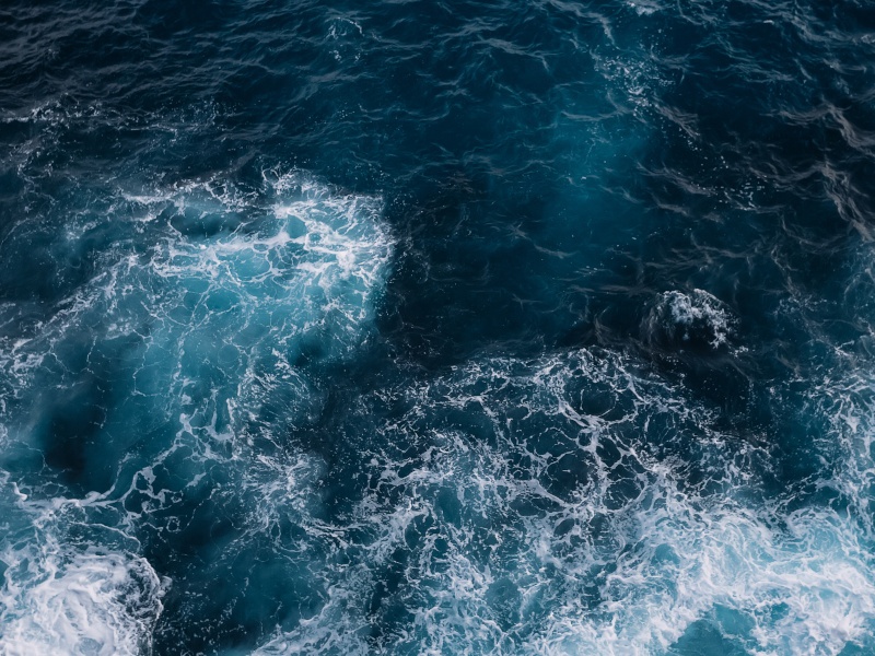 An aerial shot of the deep blue ocean with foamy waves in the foreground.