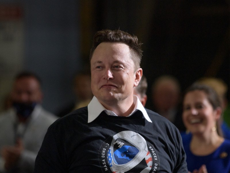 X owner Elon Musk standing in front of other people, wearing a black shirt.