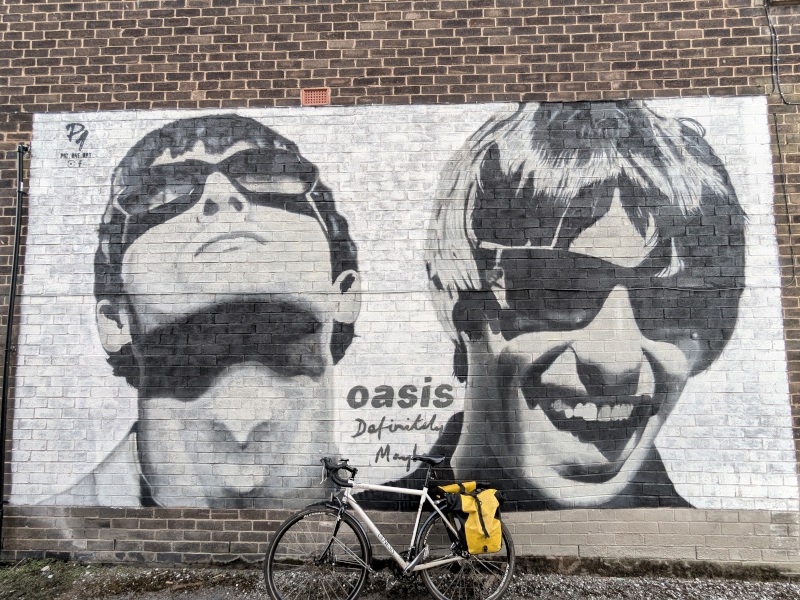 An image of the Gallagher brothers on a wall with the Oasis band name on it and a bike by the wall.