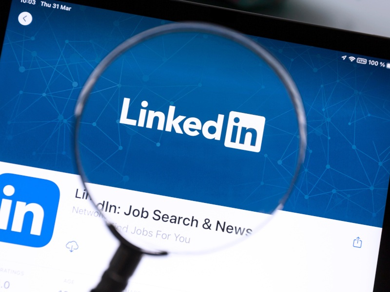 The LinkedIn logo on a website, zoomed in on by a magnifying glass.