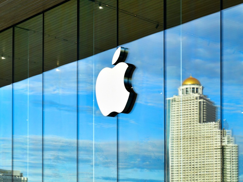 The apple logo on a glass building wall reflecting a tall building in Bangkok on a bright sunny day.