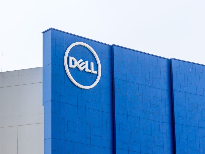 A white Dell logo on top of a large blue wall against a bright, white clouded sky.