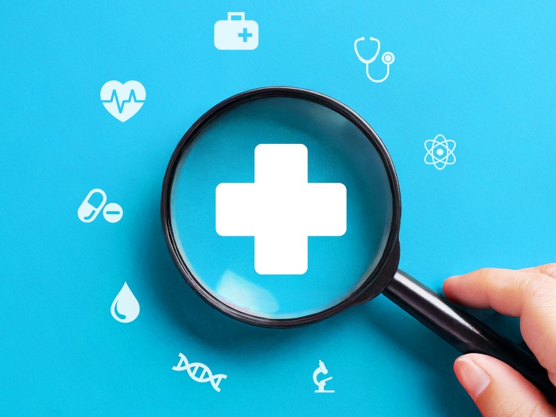 Light blue background with health related symbols in white and a magnifying glass magnifying the health cross symbol in the centre.