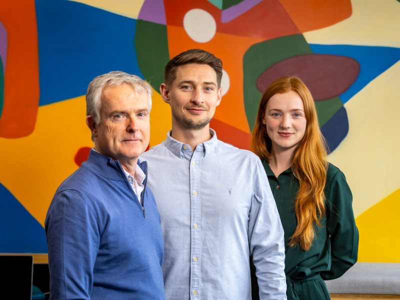 Delta Partners venture capital firm's Dermot Berkery standing with Imvizar's Michael Guerin and Adele Keane. against a colourful background.