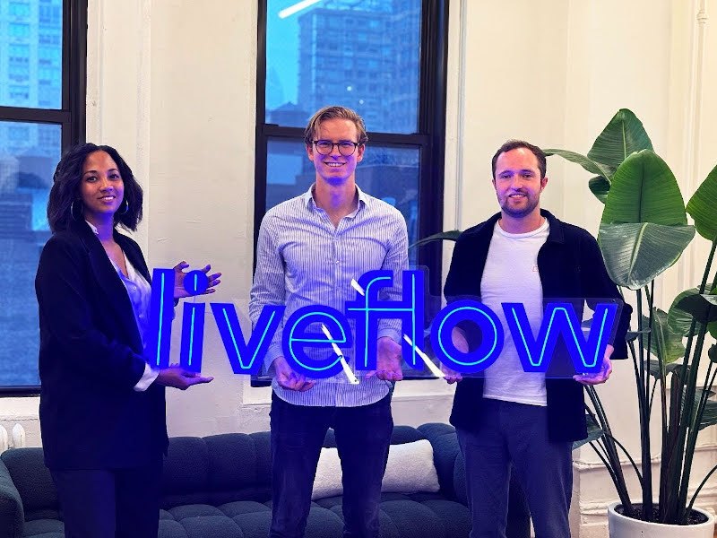 A woman and two men stand in a bright office building with a plant beside them. They are holding a blue, lit-up sign that says LiveFlow.