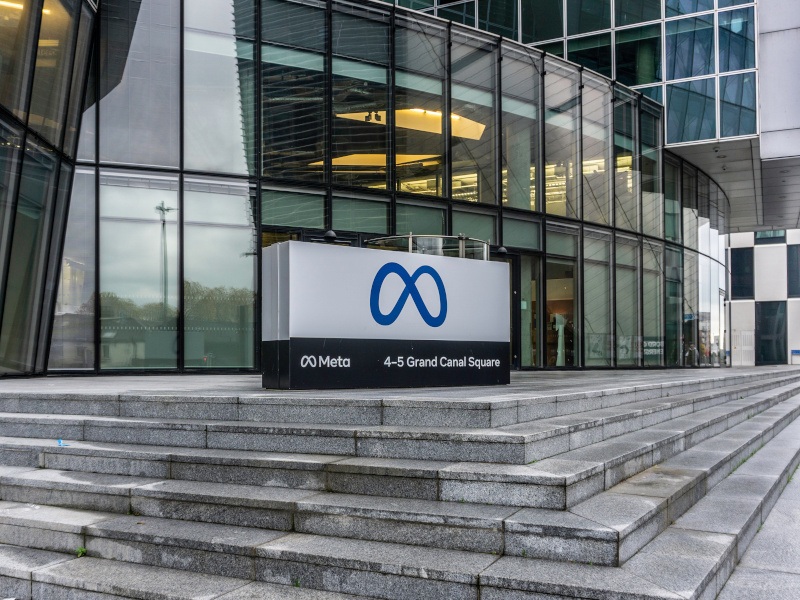 A sign showing the Meta logo at the top of steps outside a large glass office building.