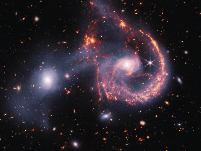 A small white galaxy and a larger red spiral galaxy next to each other in space, with white gas between them. Taken from the James Webb Space Telescope.