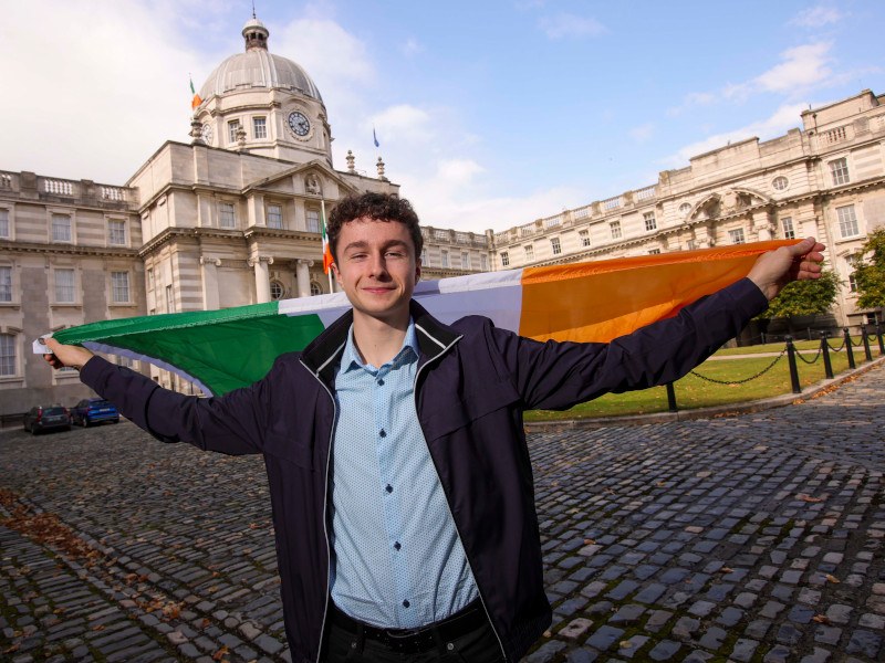 Seán O’Sullivan, second place winner of EUCYS 2024 in front of the government building in Dublin with an Irish flag on this back.