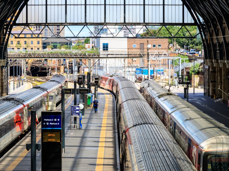 An overhead shot of trains and semi-covered platforms at King’s Cross train station in London on a sunny day.