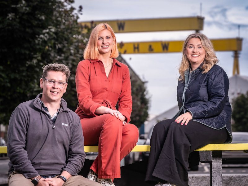 A man and two women sitting together on a yellow bench.