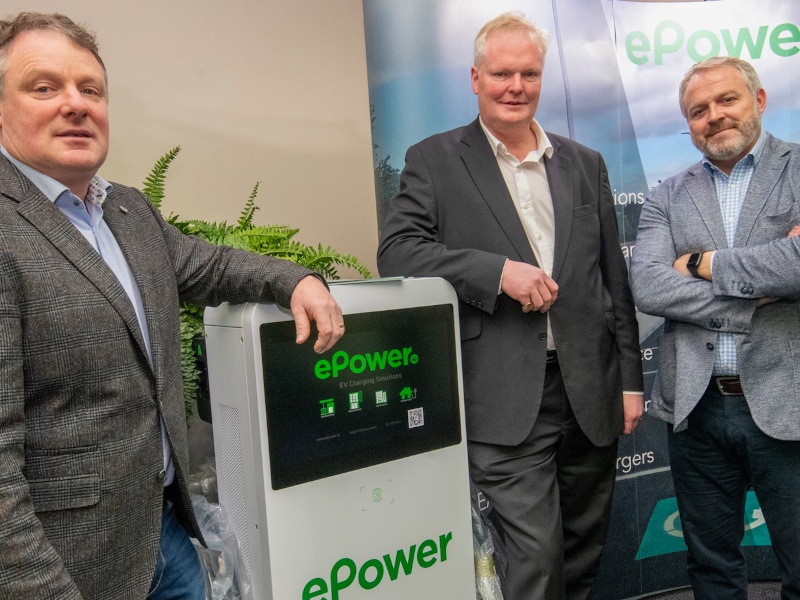 Three men standing next to an ePower electric vehicle charger in a room.