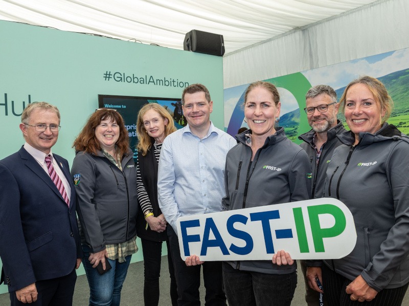 Seven people standing in a group with one woman in the middle holding a large Fast-IP sign.