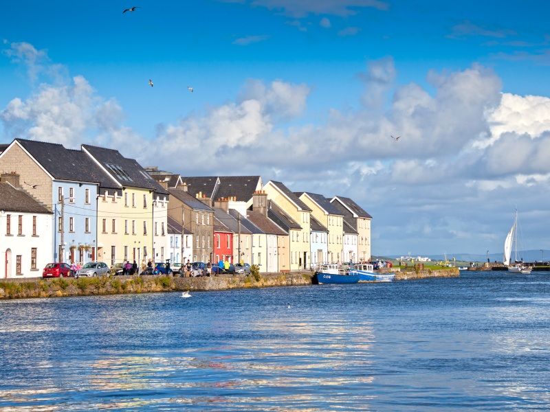 A sunny day at the Claddagh docks in Galway. A river in the foreground with colourful houses to the back.