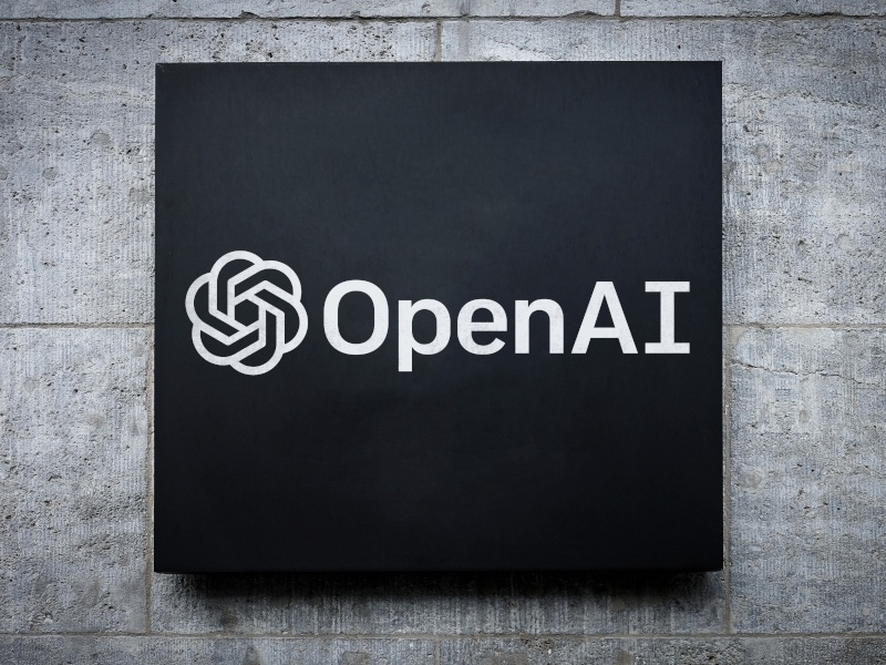 A cement grey wall and the OpenAI company logo in black and white.