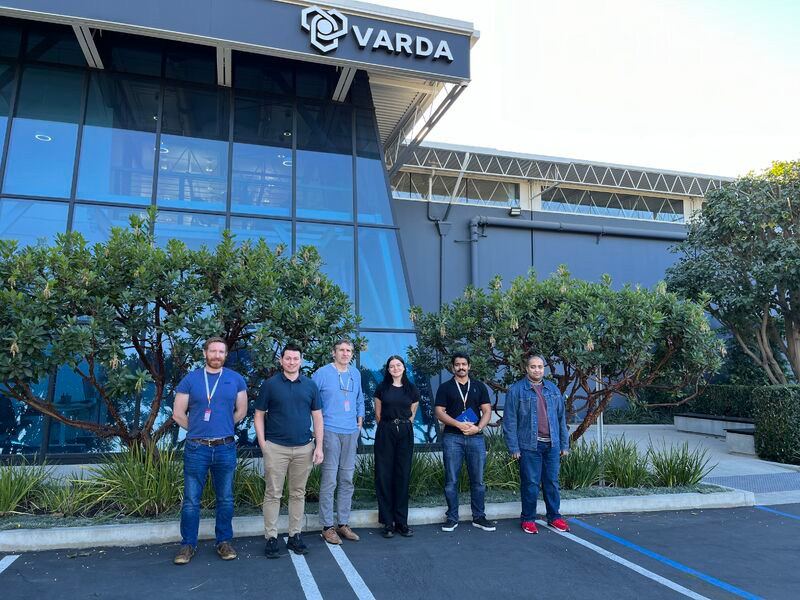 One woman and five men standing outside of a building with the Varda Space Industries logo on the side.