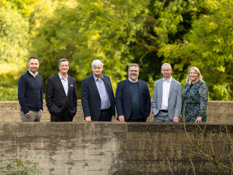 Team members meeting in green outdoor area on a bridge.