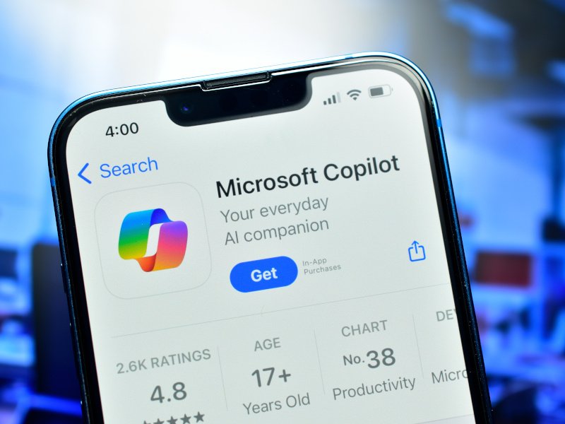 A phone with the Microsoft Copilot app on the screen against a blurred office background.