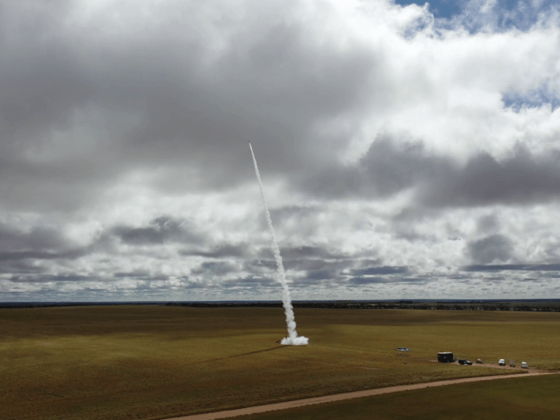 Wide cloudy sky and a small rocket launch in the middle of a wide field.