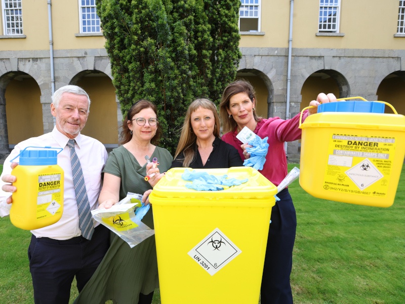 Four people standing outside holding hazardous waste containers. One man in the left and three women to the right.